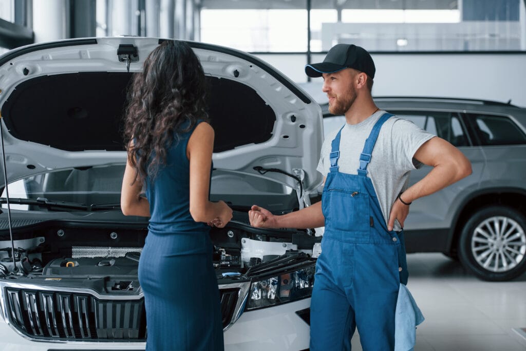 Elegant girl. Woman in the auto salon with employee in blue uniform taking her repaired car back.