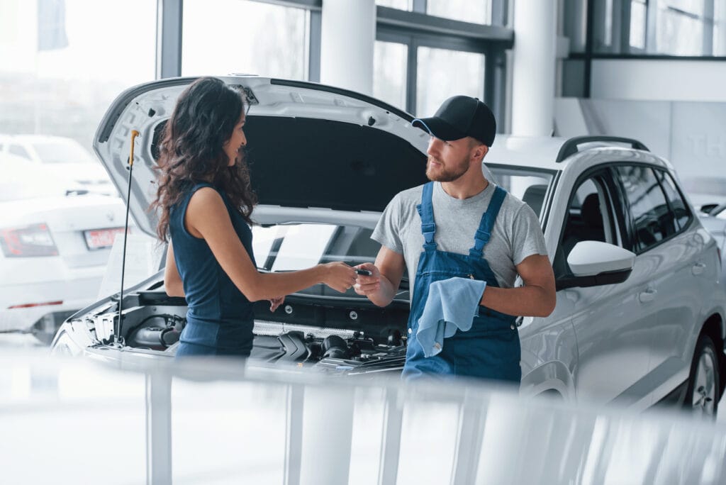 Trust and occupation. Woman in the auto salon with employee in blue uniform taking her repaired car back.